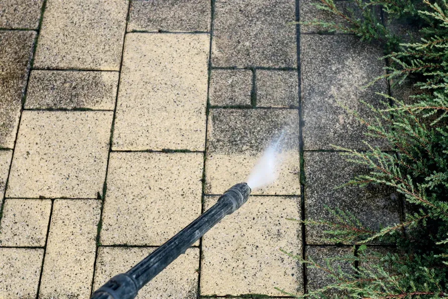 Pressure washer lance cleaning a patio, with a clean strip next to dirty, moss-covered slabs